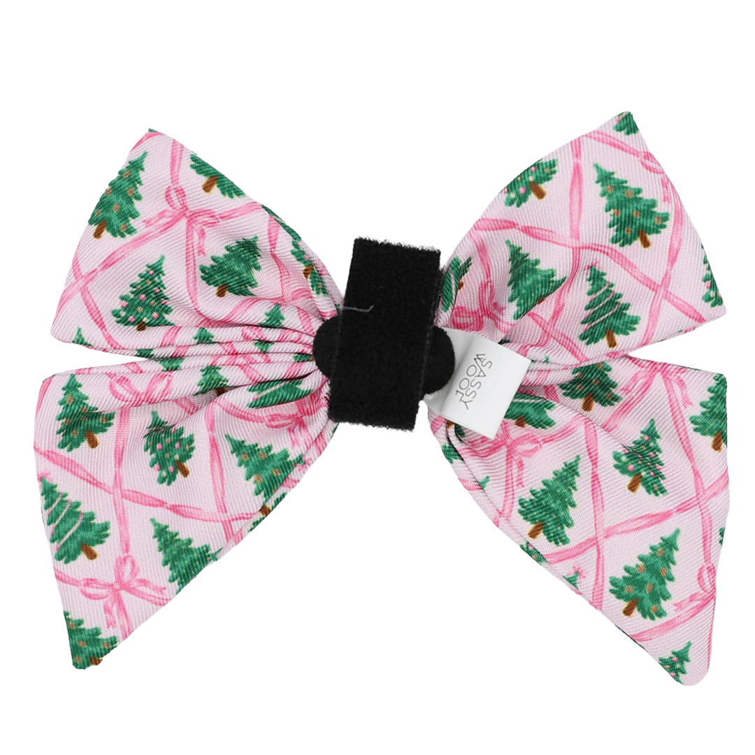 Introducing the Dog Sailor Bow - Pretty in Pine by Sassy Woof: a charming pink bow adorned with green Christmas trees and red ribbons, featuring a black center band and finished with a small white tag. This festive accessory is perfect for elevating your dog’s winter fashion or pairing seamlessly with other evergreen dog accessories.