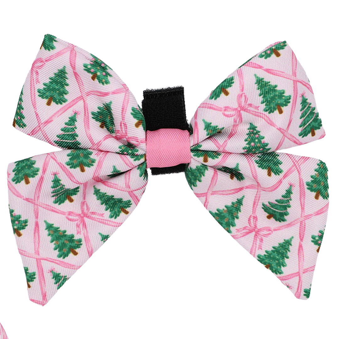 Introducing the Dog Sailor Bow - Pretty in Pine from Sassy Woof: This delightful hair bow features a pink background adorned with green Christmas trees and playful pink ribbon patterns. Accented by a stylish black and pink center band, it’s the perfect piece to elevate your pup’s seasonal accessories or add festive charm to any dog winter fashion look.