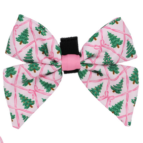 Introducing the Dog Sailor Bow - Pretty in Pine from Sassy Woof: This delightful hair bow features a pink background adorned with green Christmas trees and playful pink ribbon patterns. Accented by a stylish black and pink center band, it’s the perfect piece to elevate your pup’s seasonal accessories or add festive charm to any dog winter fashion look.