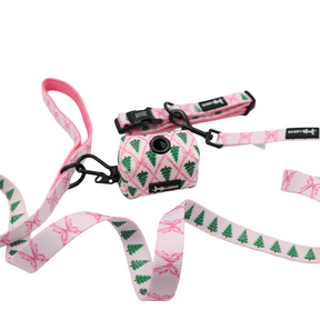 Sassy Woof’s Dog Collar Three Piece Bundle - Pretty in Pine features a pink and white winter-themed set, including an evergreen dog leash, a Pretty in Pine dog collar, and a coordinating waste bag holder adorned with charming Christmas tree and bow designs, all beautifully displayed on a white background.