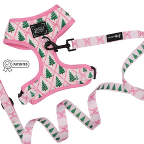 Introducing the Sassy Woof Dog Two Piece Bundle - Pretty in Pine, an adjustable dog harness and leash set from the Pretty in Pine collection. Showcasing vibrant green Christmas trees and charming pink ribbon patterns, this bundle is perfect for winter dog accessories. The harness features signature Sassy Woof branding, a secure black leash clip, and a Patented icon on the left.