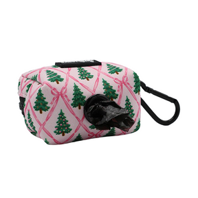 Introducing the Sassy Woof Dog Waste Bag Holder - Pretty in Pine: a pink neoprene bag holder adorned with charming Christmas tree and bow designs, featuring a convenient black dispenser opening with a bag visible and an attached black carabiner clip—perfect for pairing with your favorite winter accessories from the Evergreen Dog Collection.