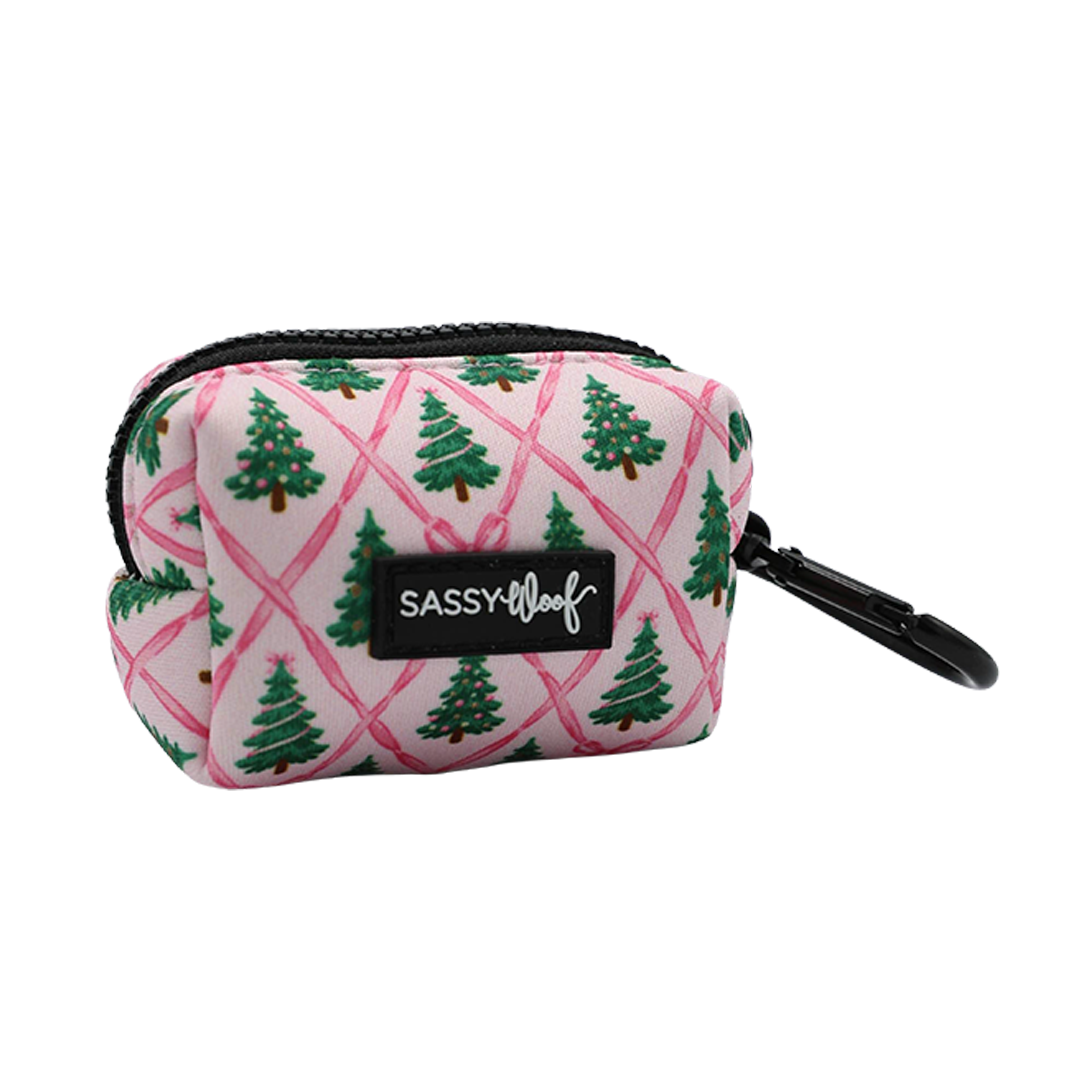 Introducing the Dog Waste Bag Holder - Pretty in Pine by Sassy Woof. This small pink neoprene bag features a festive repeating Christmas tree pattern, a black zipper, and a sturdy black clip for easy attachment. The front is adorned with a signature Sassy Woof label in black. Part of the Evergreen Dog Collection, this stylish and functional accessory adds both charm and practicality to your dog’s winter essentials.
