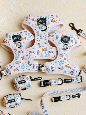 Three Sassy Woof Dog Four Piece Bundles from the Weenie Wonderland Collection are displayed on a light textured background. Each bundle includes a pastel pink adjustable harness with whimsical cartoon dog and winter tree patterns, a matching collar, leash, and small bag holder—perfectly crafted for both comfort and style as an ideal dachshund harness.