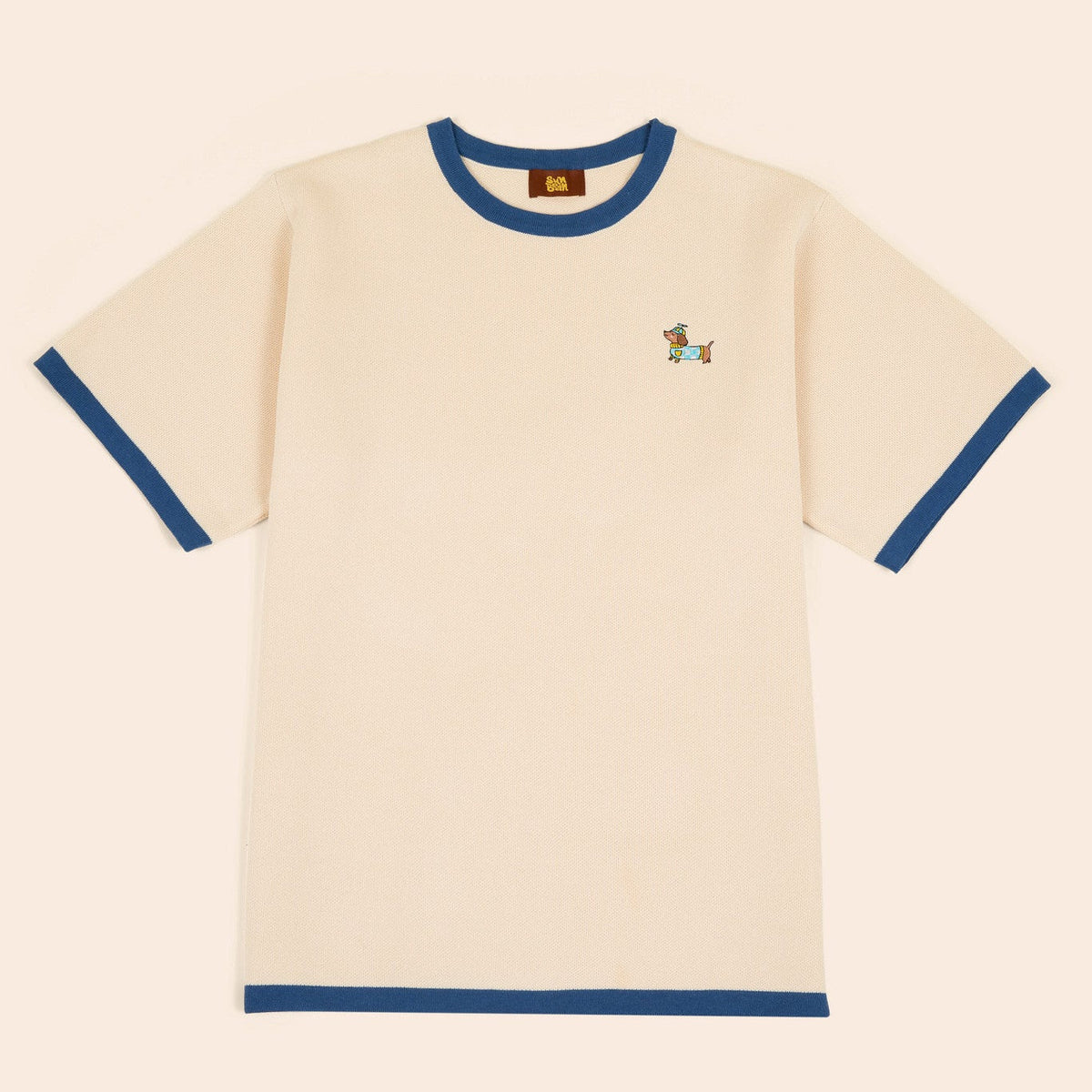 The Sassy Woof x Sunbean Human Tee by Sunbean is a beige short-sleeve t-shirt with blue collar and sleeve cuffs, featuring a small embroidered dog on the left chest.