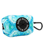 The Sassy Woof Dog Waste Bag Holder - Tropical Tides features blue and green neoprene, a black circular dispenser, and a clip for easy attachment—perfect for adding a stylish tropical touch to your dog walks.