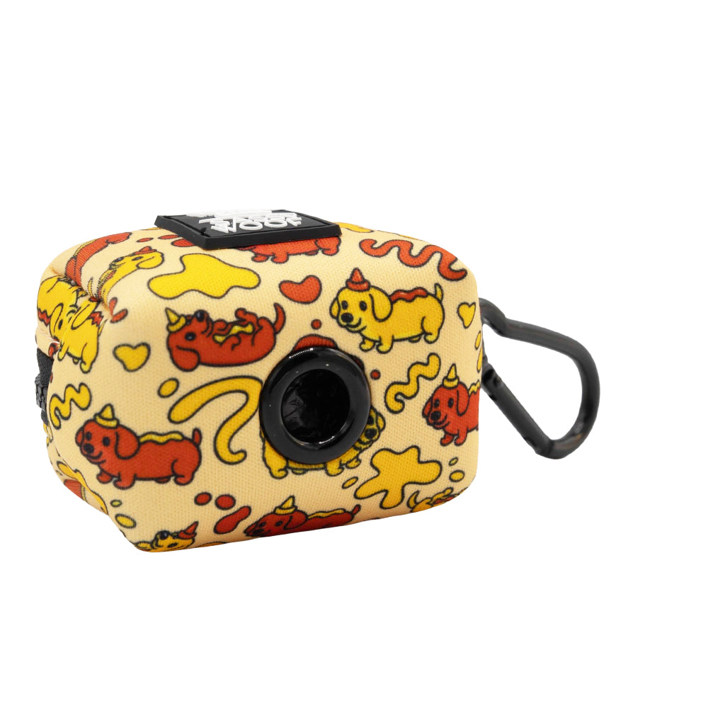 The Sassy Woof Dog Three Piece Bundle - Hot Dawg features a small, rectangular yellow pouch with red and yellow cartoon corgis, playful squiggles, a black clip, and a front circular opening for waste bag dispensing.