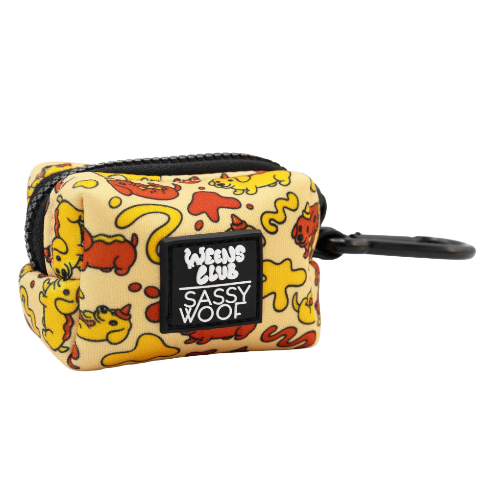 The Dog Waste Bag Holder - Hot Dawg by Sassy Woof is a small rectangular pouch with a yellow, red, and orange dog cartoon print, zipper, black clip, and "Weens Club Sassy Woof" patch—ideal for holding waste bags or dachshund accessories.