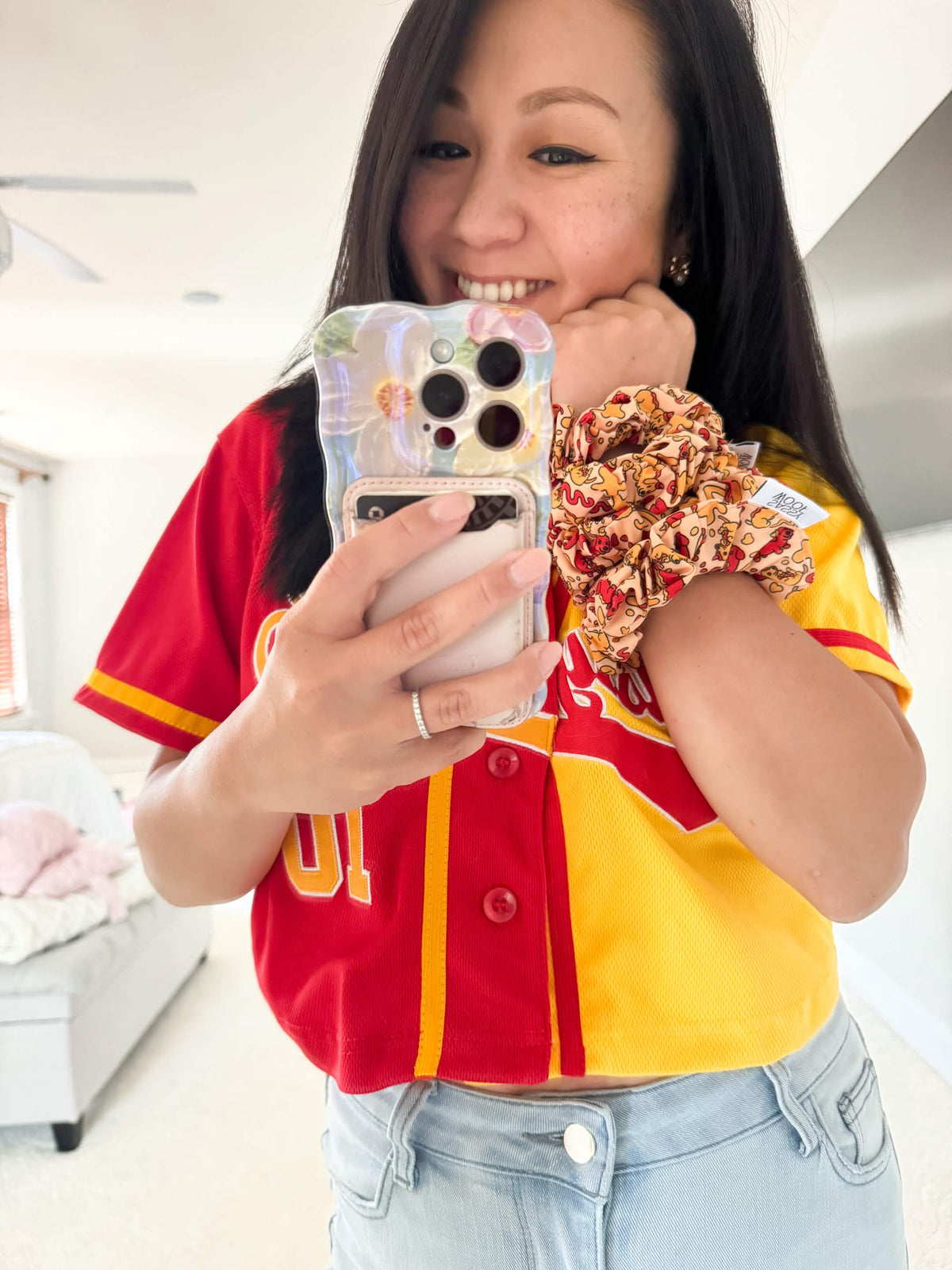 A smiling woman takes a mirror selfie, wearing the Hot Dawg - Scrunchie by Sassy Woof on her wrist. Her playful style shines through, making it a perfect pick for Yuna Bugs x Sassy Woof fans.