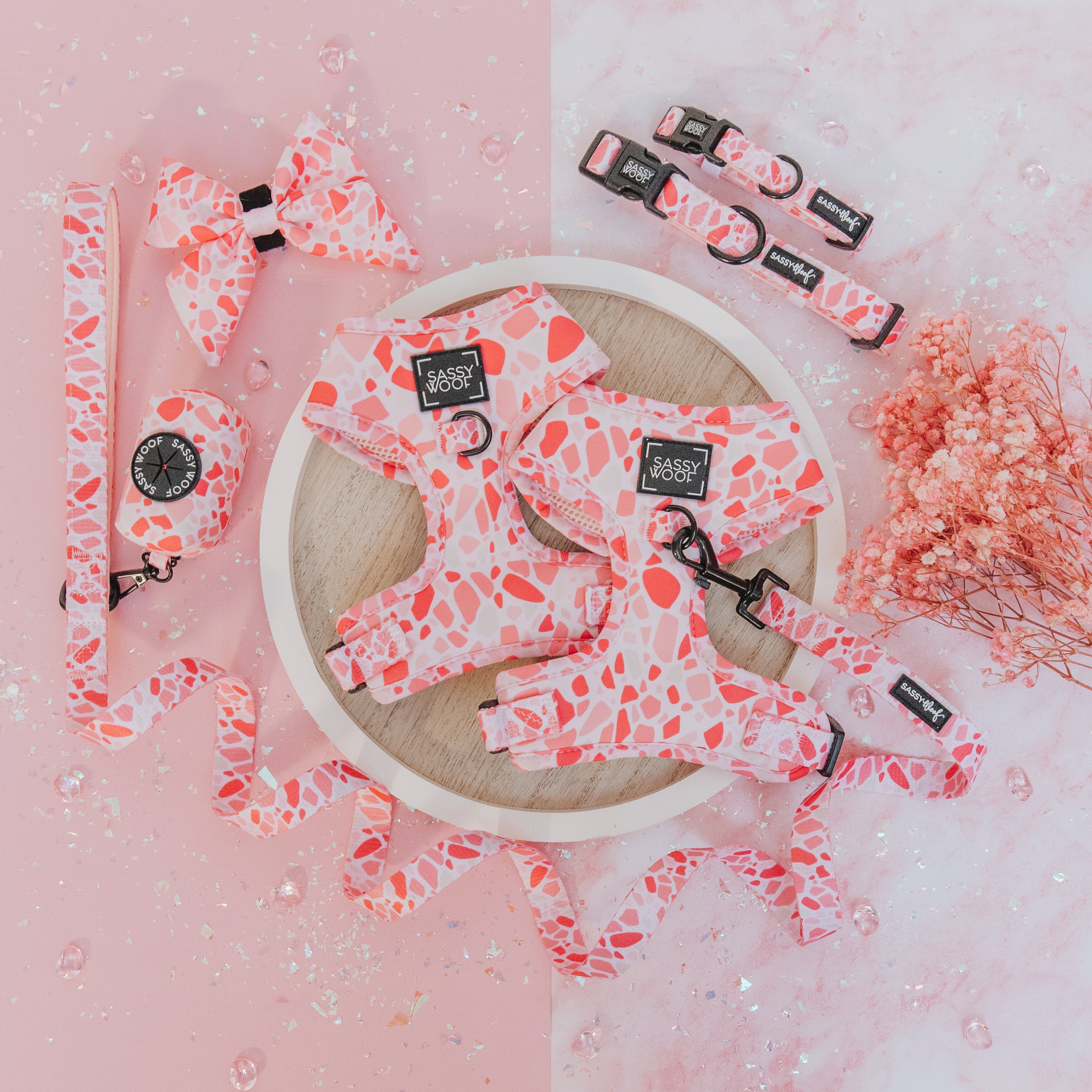 The Sassy Woof Dog Four Piece Bundle - Mykonos features pink and coral speckled dog accessories, beautifully arranged on a wooden tray with flowers and sparkling gems against a pink marble background.