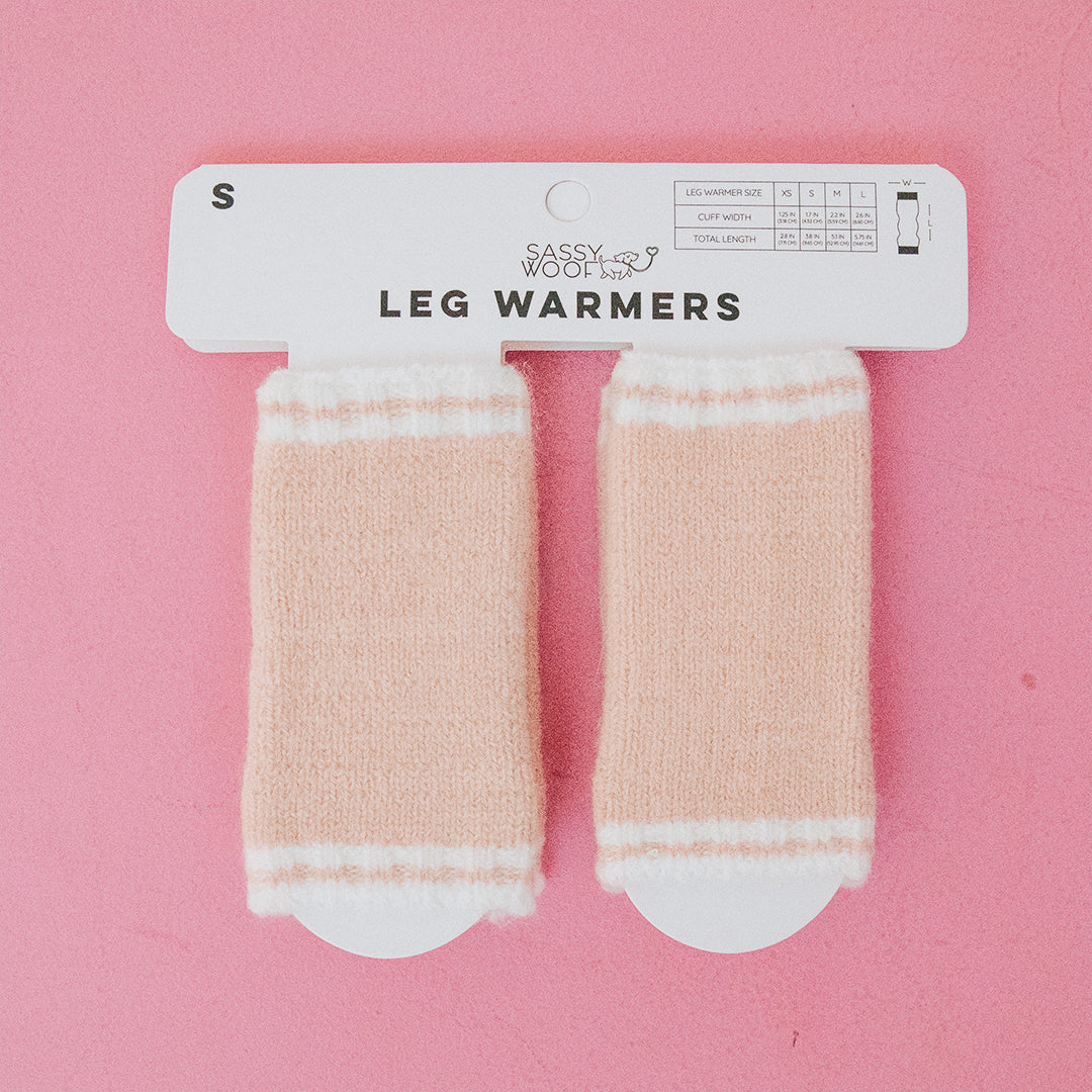 A pair of small pink Sassy Woof Dog Leg Warmers made from soft acrylic with white stripes, displayed on a hanger—perfect cold weather accessories for your pup.