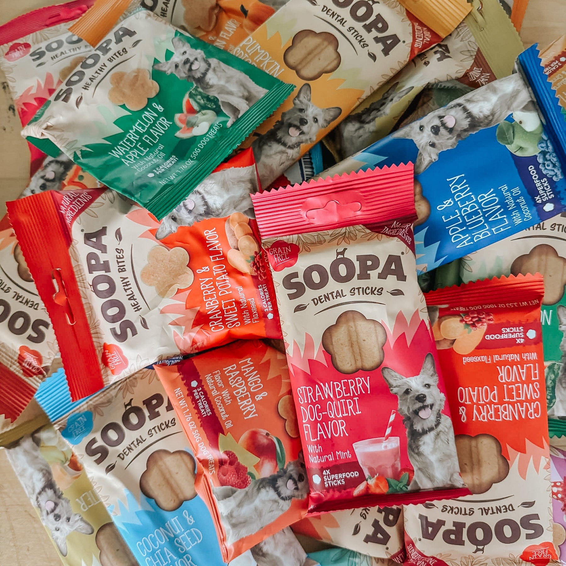A pile of Sassy Woof Soopa Treat Bags in colorful, hypoallergenic, grain-free packaging with cartoon dogs and flavor labels like strawberry, coconut, carrot, and apple.