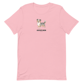 The Aussie Mom Tee by Sassy Woof is a light pink unisex shirt with an illustrated Australian Shepherd and bold black lettering, made from eco-friendly cotton—perfect for stylish, proud dog parents.