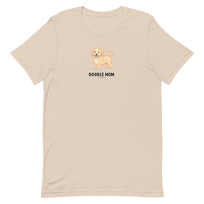 The Doodle Mom Tee by Sassy Woof is a beige unisex shirt featuring a small, smiling dog illustration above bold DOODLE MOM text—perfect for any proud Doodle mom.