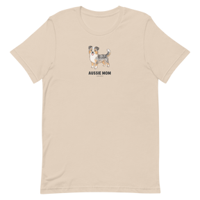 The Sassy Woof Aussie Mom Tee is a beige unisex shirt with an Australian Shepherd illustration above bold text, made from soft, eco-friendly cotton for comfort and style.
