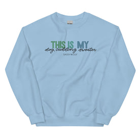 The Sassy Woof "This is My Dog Cuddling Sweater" is a light blue unisex crewneck sweatshirt featuring the phrase in green, blue, and black fonts on the front.